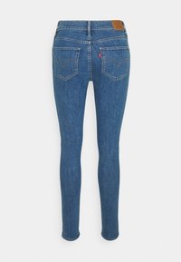 Vaqueros de denim azul ajustados con una cintura alta, bolsillo trasero con parche y detalles de costura curva. Textura suave y forma ceñida.
