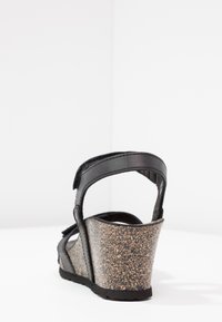 Sandalo con zeppa nera e tacco in sughero, cinturino regolabile e morbidi dettagli in tessuto nero. Vista posteriore che evidenzia la forma e i materiali.