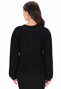 Schwarzer Strickpullover mit strukturiertem Muster, ausgestattet mit einem gerippten Kragen und Bündchen, die entlang des Halsausschnitts dezent mit Perlen verziert sind.