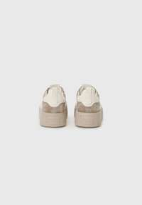Beige suedetreningssko med kremfargede lærdetaljer, polstret krage og tykke gummisåler. Bakre håndtak for enkel påsetting. Strukturert overflate.
