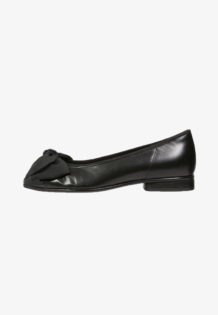Ballerine plate en cuir noir avec un petit talon et un grand nœud en tissu sur le bout arrondi, vue de profil.