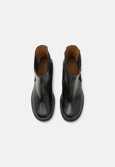 Botas de cuero negro hasta el tobillo con paneles laterales elásticos, puntera redonda y una textura suave. El interior tiene un forro marrón.