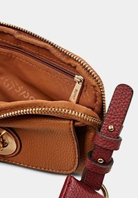 Interno di una borsa a spalla in pelle marrone con una tasca con zip, hardware dorato e tracolla bordeaux. Finitura texturizzata e scomparto foderato visibili.
