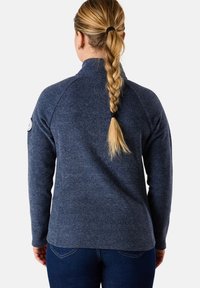 Pullover in pile di colore blu navale con colletto alto, tessuto testurizzato e maniche raglan. Presenta una toppa con logo sulla manica sinistra.
