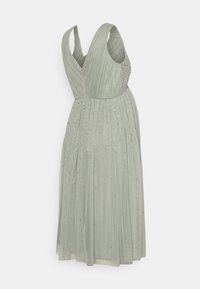 Vestido verde plissado com decote em V e alças largas, adornado com pequenos enfeites prateados, design fluido e comprimento até o joelho.