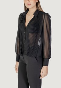 Blusa nera plissettata con scollatura a colletto, in tessuto traslucido, con bottoni frontali e maniche lunghe a sbuffo. Design strutturato e fluttuante.