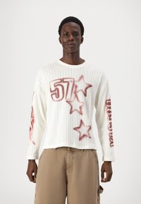 Maglione bianco a maniche lunghe in maglia con stampe grafiche rosse del numero "57" e forme a stella, con scollo a girocollo e trama a coste.