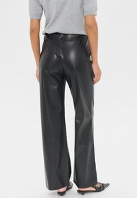 Pantalones de cuero sintético negros de pierna ancha con cintura alta, textura suave y costuras mínimas, combinados con bailarinas negras de punta afilada.