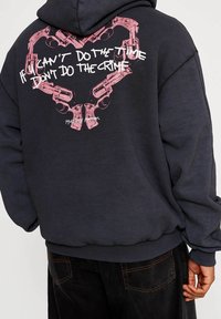 Felpa grigia scura con un design grafico rosa che rappresenta pistole disposte a forma di cuore, con il testo: "Se non puoi scontare la pena, non commettere il reato."