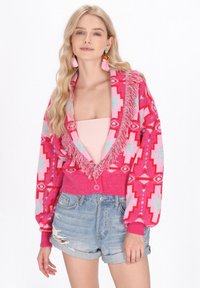 Cardigan a fantasia rosa e blu con frange, design corto e chiusura a bottoni, abbinato a pantaloni scampanati in denim strappati.