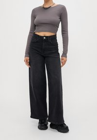 Grå långärmad kort topp kombinerad med högmidjade, vida svarta jeans. Har knappstängning och textilstruktur. Bärs med svarta skor.