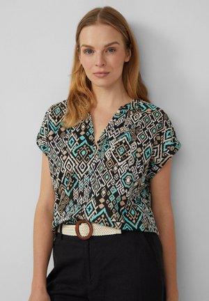 Blouse à manches courtes avec un motif géométrique noir, crème et turquoise, dotée d'un décolleté en V et d'une coupe décontractée. Accentuée par une ceinture de couleur claire.