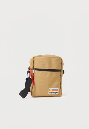 Petit sac bandoulière beige avec fermeture éclair noire, tirettes rouges, sangle noire réglable et patch coloré "montagne" sur le devant.