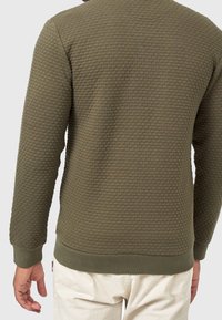 Sweatshirt texturé vert olive avec un motif matelassé, poignets et ourlet côtelés, et col rond. Détails de coutures apparentes.