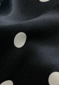 Gros plan d’un tissu noir à pois blancs montrant une texture lisse et des plis doux.