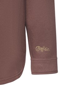 Brown long-sleeve shirt with a soft texture, featuring rolled cuffs and a gold embroidered logo on the sleeve.