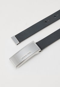 Juodas odinis diržas su sidabriniu stačiakampiu sagtimi, kuriame išgraviruota „MICHAEL KORS“, ir elegantiška, lygi tekstūra. Matomos dvi galinės dalys.