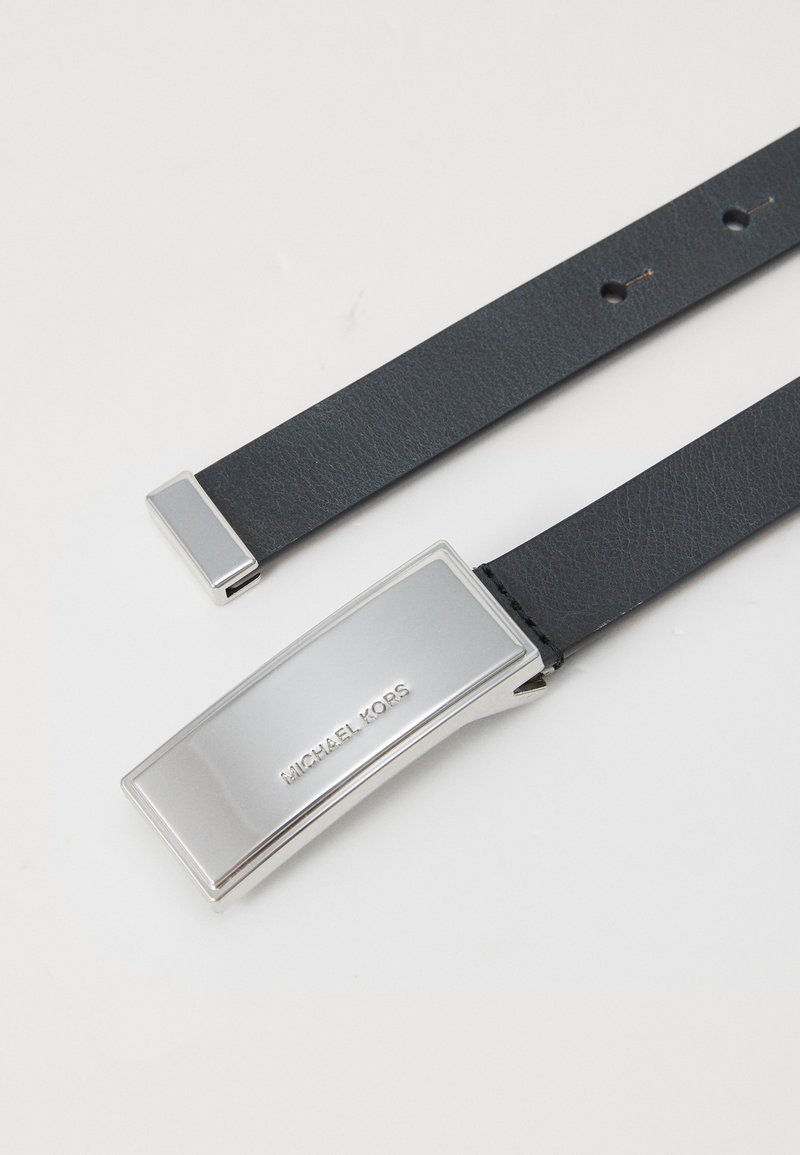 Cintura in pelle nera con una fibbia rettangolare argentata incisa con 'MICHAEL KORS' e una texture liscia e elegante. Due estremità visibili.