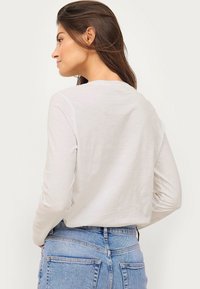 Hvid langærmet T-shirt med en rund halsudskæring, blød tekstur og en afslappet pasform, parret med lyseblå jeans med baglommer.