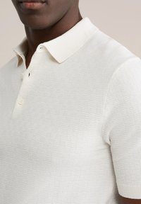 Wit gebreid poloshirt met een textuurpatroon, voorzien van een zachte kraag, korte mouwen en drie knopen bij de hals.