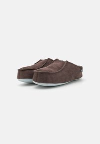 Chaussons en suède marron avec une forme arrondie, présentant un empeigne pliée autour de l'ouverture et une semelle gris clair. Design simple, sans motifs visibles.