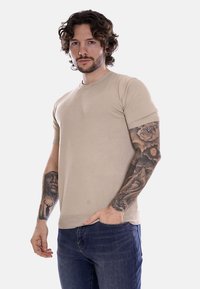 T-shirt beige a maniche corte con scollatura rotonda e texture a costine. Presenta un design aderente, abbinato a jeans in denim.
