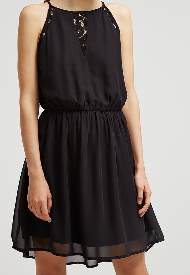 Robe en chiffon noire avec un corsage ajusté, des accents de dentelle sur les épaules et une taille élastique. Jupe fluide avec une légère brillance.