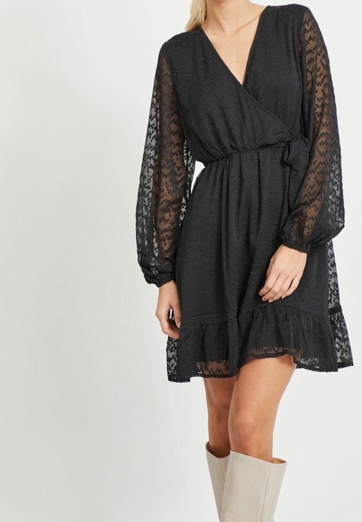 Svart omlottklänning med långa genomskinliga ärmar, texturerad tyg, midja med bälte och rynkad fåll. Accenterad med ett spetsmönster.
