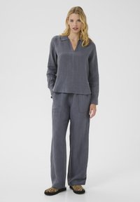 Haut long en lin gris avec un décolleté en V et une coupe légèrement décontractée, associé à un pantalon large assorti doté de poches avant.