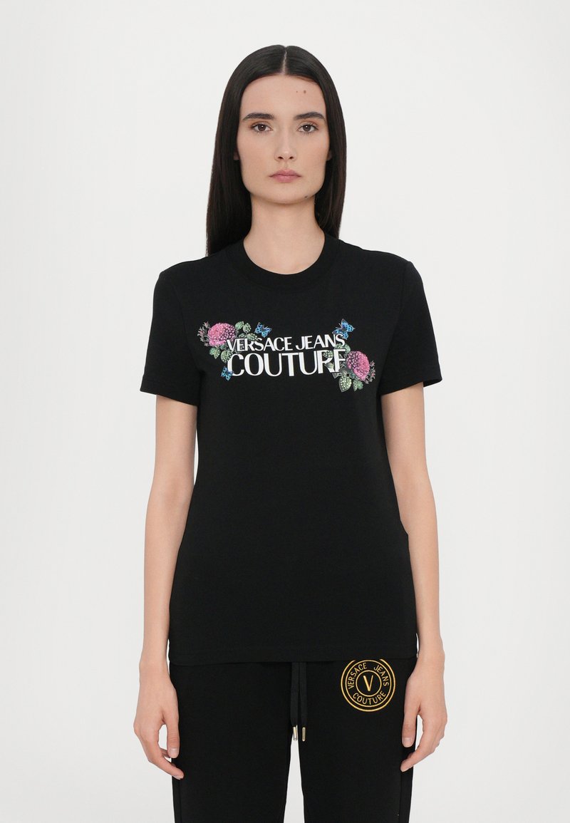 Juodas trumpaapykaklis marškinėliai, puošiami gėlių siuvinėjimu ir baltu "VERSACE JEANS COUTURE" logotipu. Minkšta medvilnė. Standartinė fasonas.