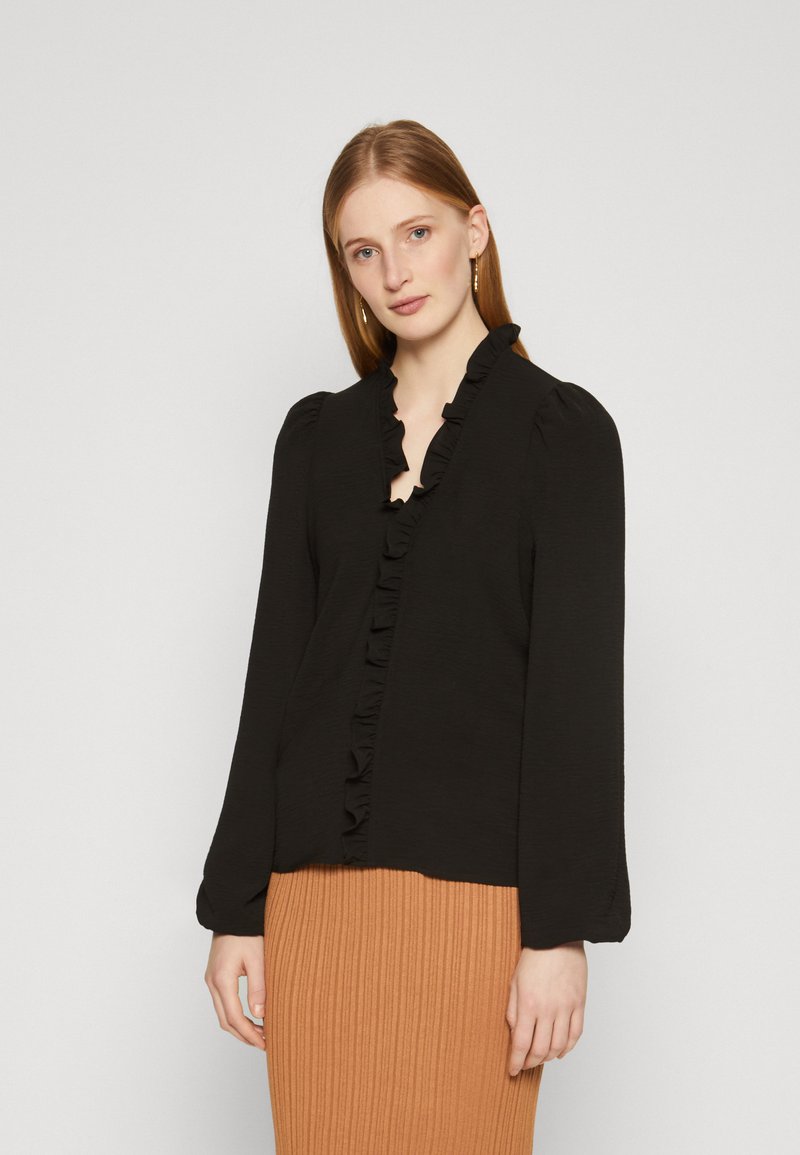 Black long-sleeve blouse with ruffled neckline and cuffs, featuring a smooth texture, paired with a ribbed brown skirt for contrast.