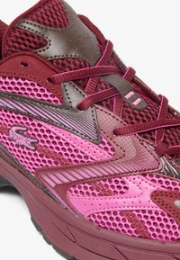 Zapatilla de running en rosa y burdeos que presenta materiales de malla y sintéticos, forma redondeada, acentos texturizados y cordones en contraste.