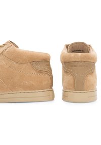 Zapatillas de ante en color arena con un diseño de caña alta, cuello acolchado y suela de goma beige en contraste. Presentan acentos de costura y marca en el costado.