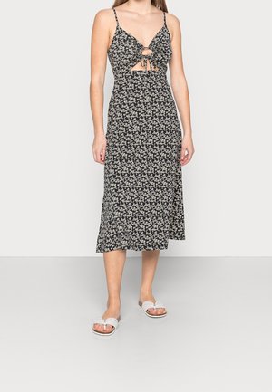 Schwarzes Blumenkleid mit Spaghettiträgern, Ausschnitt vorn und midilangem Rock. Kombiniert mit weißen Flip-Flops mit schlichtem Design.