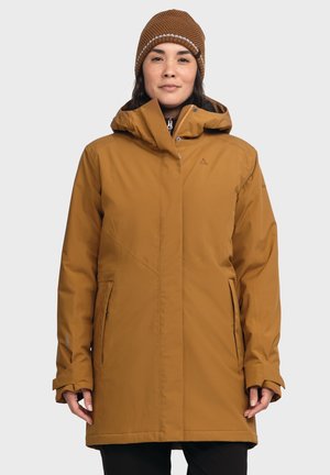 Braune isolierte Jacke mit Kapuze, ausgestattet mit Fronttaschen, einem Reißverschluss und einem eleganten Design. Getragen mit einer strukturierten braunen Strickmütze.