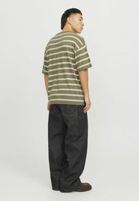 Olivenfarvet stribet t-shirt med korte ærmer; parret med mørk denim, løstsiddende cargo bukser; har en lige pasform og minimal detaljer.