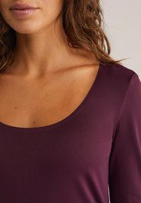 Bordo ilga rankovė viršutinė dalis su plačiu apvaliu kaklu, minkšta tekstūra ir prigludusia siluetu, parodanti lygų audinį be raštų ar detalių.