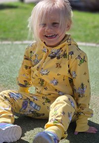 Gul zip-up träningsdräkt med olika tryck av tecknade djur, tillverkad av mjukt tyg med en perfekt slät yta. Inkluderar byxor och en huva.