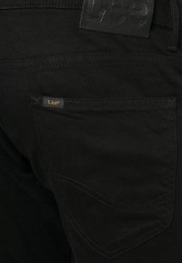 Svarta jeans i ett strukturerat tyg, med en bakficka och en läderetikett präglad med logotypen "Lee."