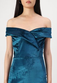 Teal haljina bez rukava od mekanog baršuna. Ima dizajn omotane bustier i glatku teksturu s uskim siluetom.