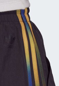 Černé atletické šortky s třemi svislými pruhy v žluté, modré a zelené barvě. Materiál působí lehce a má jemný lesk.