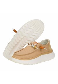 Scarpe slip-on in tela beige con una suola bianca spessa, caratterizzate da una trama intrecciata, perline decorative e un piccolo tassello marrone.