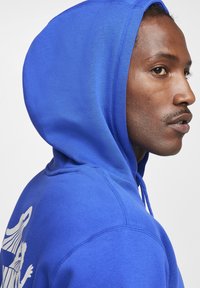 Royalblauer Hoodie aus weichem Material, mit Kapuze und Kordelzug sowie einem weißen Grafikdesign auf der Rückseite. Glatte Textur und mittlere Passform.