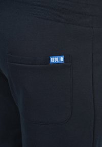 Navy jogger pants with a back pocket featuring a ribbed texture. A blue label with the text "ISOLID" is visible on the pocket.