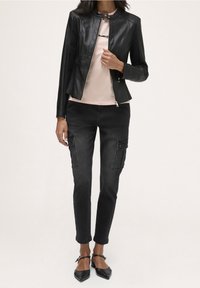 Svart läderjacka med en figurnära design, i kombination med en ljusrosa blus, svarta cargobyxor och svarta platta skor med ankelrem.