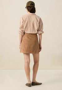 Brown corduroy skirt with a straight design, paired with a striped beige and rust shirt and a leopard-print cap. Textured flat shoes complete the look.