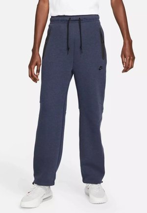 Pantaloni della tuta blu scuro con vita regolabile con coulisse, caratterizzati da tasche con zip nere e un logo nero discreto sulla coscia. Tessuto morbido e strutturato.