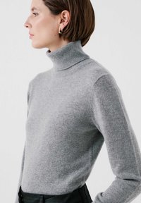 Grå polotröja i mjukt stickat material, åtsittande design med långa ärmar, med hög halslinning och jämn yta.