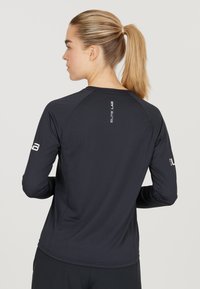 Mustassa, pitkähihaisessa urheilupaidassa on tiukka muotoilu. Siinä on raglan-hihat, sileä rakenne ja "ELITE LAB" -logo selässä ja hihoissa.