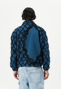Fleece jacket in blue with a textured black net pattern. Oversized fit with a high collar and dropped shoulders; soft, fluffy material.